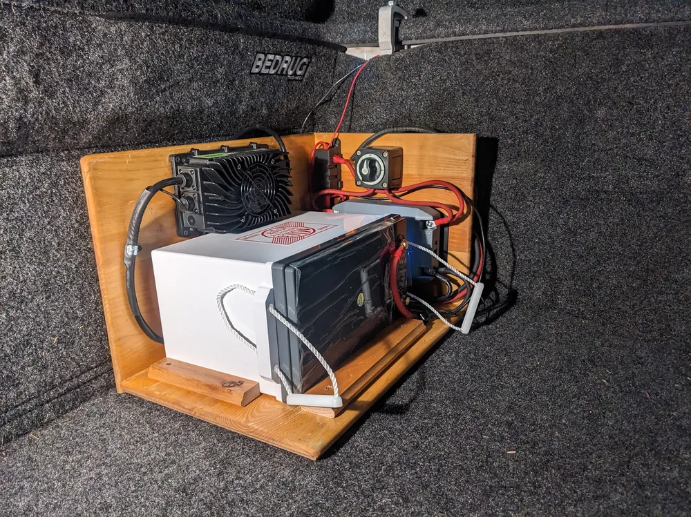 12V portable power build mounted on a wood board in a truck bed with battery, DC-DC charger, fuse, and disconnect switch